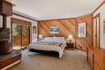 Experience cozy mountain living in this charming bedroom featuring a rustic stone fireplace and a sliding glass door leading to a private deck with forest views.