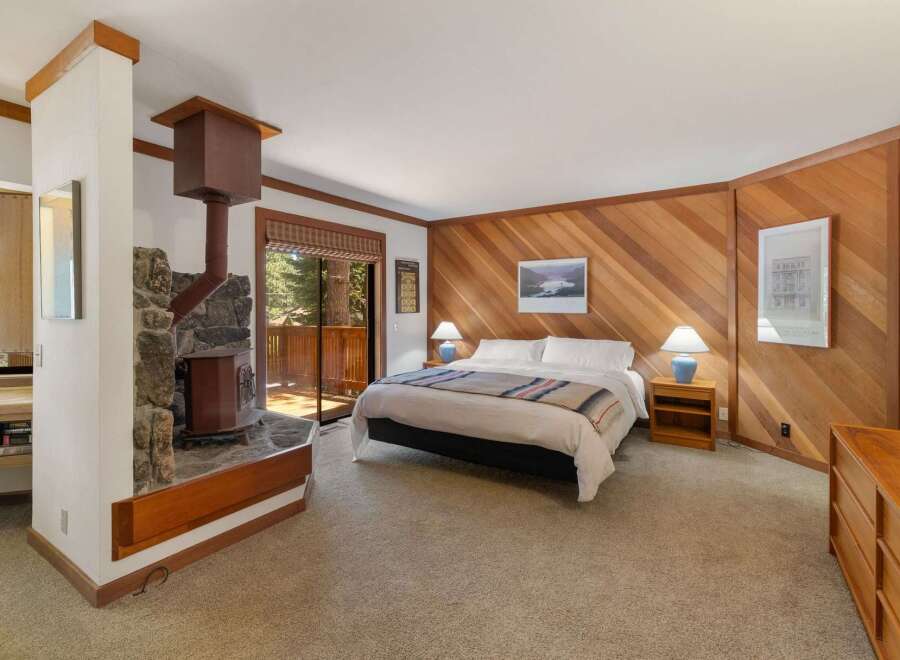 Experience cozy mountain living in this charming bedroom, featuring a striking stone fireplace with a rustic wood stove.