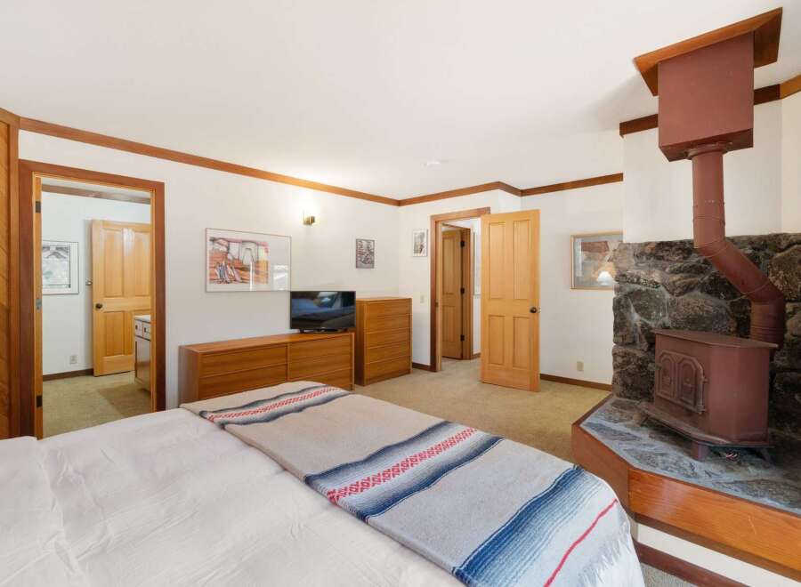 Experience cozy living in this charming bedroom featuring a rustic stone fireplace with a wood-burning stove, perfect for chilly evenings.