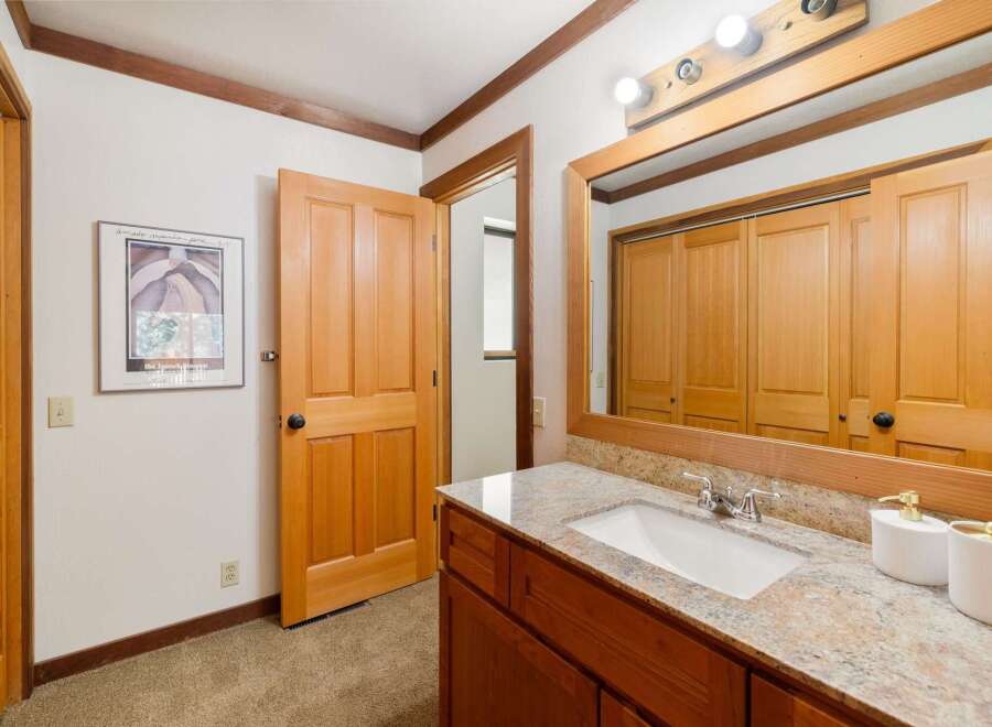 This bathroom features a spacious vanity with a granite countertop and a white undermount sink, complemented by a large mirror reflecting the wooden closet doors.