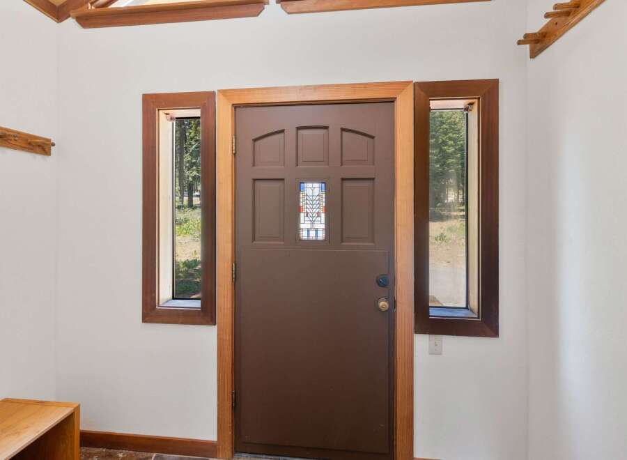 Step into this charming entryway featuring a warm brown door with a decorative stained-glass window, flanked by two inviting windows that offer views of the surrounding nature.