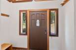 Step into this charming entryway featuring a warm brown door with a decorative stained-glass window, flanked by two inviting windows that offer views of the surrounding nature.