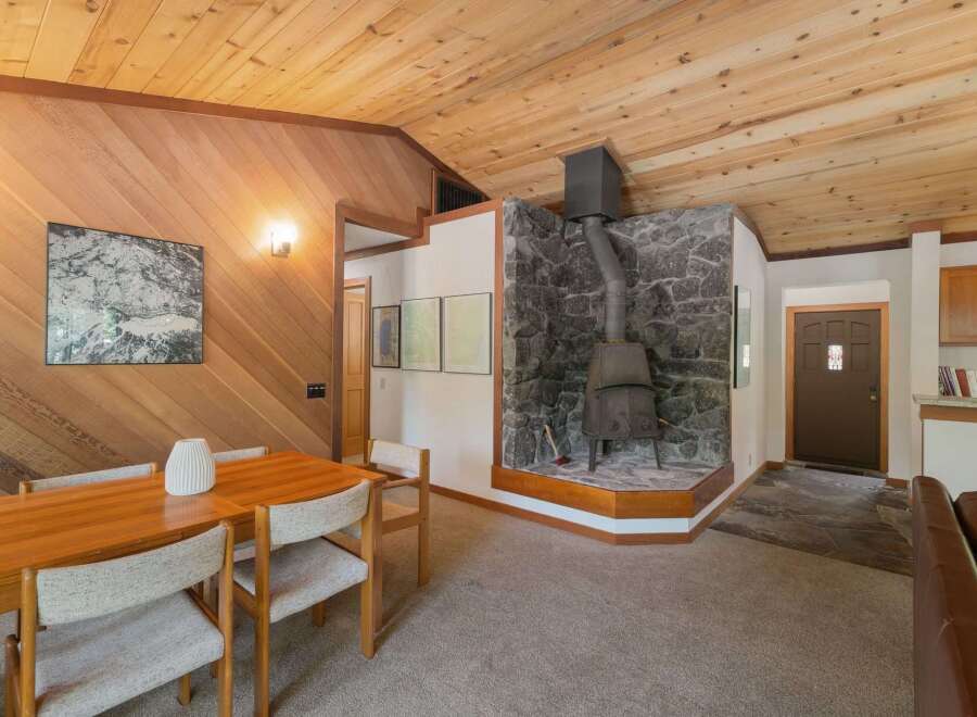 Experience cozy living in this charming dining area featuring a rustic stone fireplace with a wood-burning stove, perfect for gathering on cool evenings.