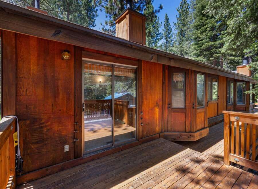 Experience rustic charm in this wooden cabin, featuring a spacious deck perfect for outdoor living and surrounded by lush pine trees.