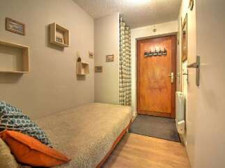 Discover this cozy studio apartment featuring a comfortable single bed adorned with decorative pillows, perfect for relaxation.