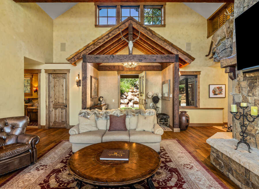 Experience rustic luxury in this stunning living room, featuring a grand stone fireplace and a soaring wooden-beamed ceiling.
