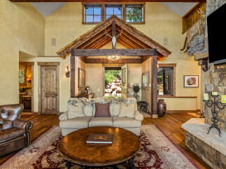 Experience rustic luxury in this stunning living room, featuring a grand stone fireplace and a soaring wooden-beamed ceiling.