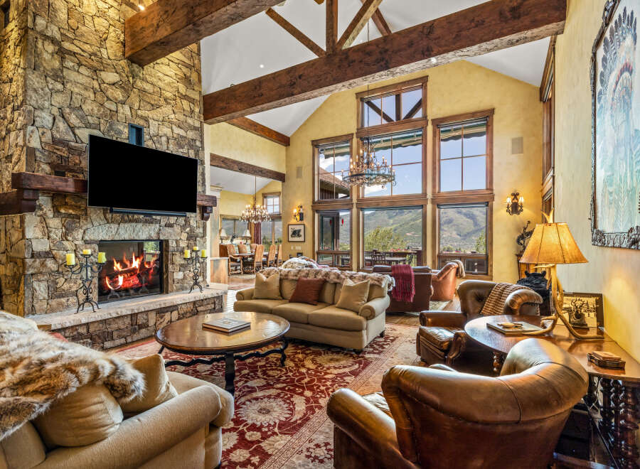 Experience luxurious mountain living in this stunning great room, featuring a grand stone fireplace and soaring vaulted ceilings with exposed wooden beams.
