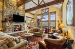Experience luxurious mountain living in this stunning great room, featuring a grand stone fireplace and soaring vaulted ceilings with exposed wooden beams.