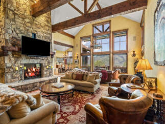Experience luxurious mountain living in this stunning great room, featuring a grand stone fireplace and soaring vaulted ceilings with exposed wooden beams.