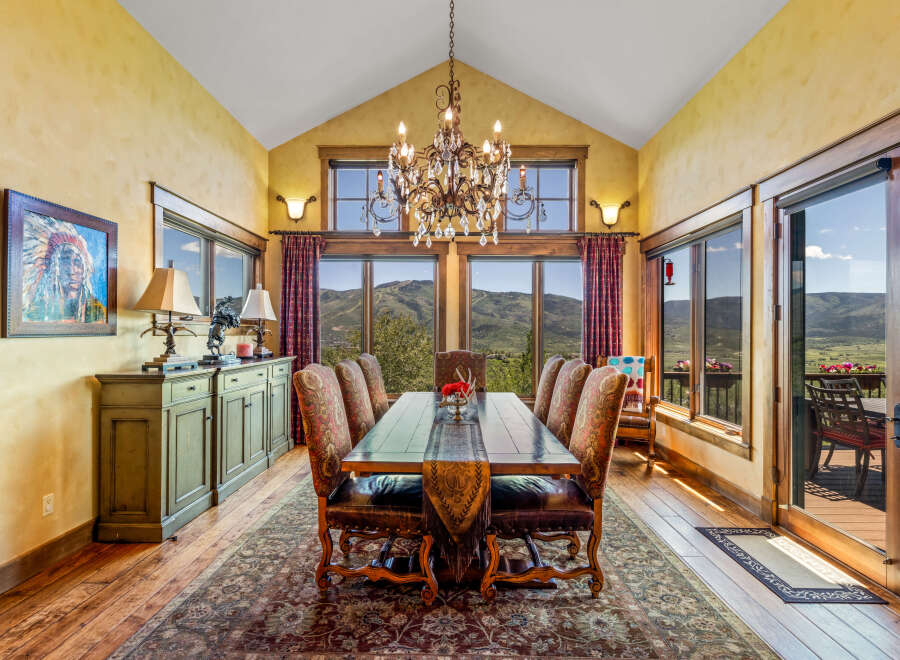 Experience breathtaking mountain views from this elegant dining room, featuring a grand crystal chandelier and a rustic wooden table set for intimate gatherings.