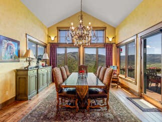 Experience breathtaking mountain views from this elegant dining room, featuring a grand crystal chandelier and a rustic wooden table set for intimate gatherings.