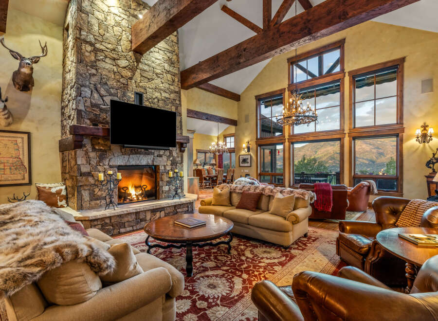 Experience luxury mountain living in this stunning great room, featuring a grand stone fireplace and soaring vaulted ceilings with exposed wooden beams.