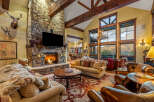 Experience luxury mountain living in this stunning great room, featuring a grand stone fireplace and soaring vaulted ceilings with exposed wooden beams.