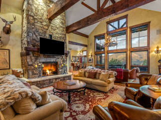 Experience luxury mountain living in this stunning great room, featuring a grand stone fireplace and soaring vaulted ceilings with exposed wooden beams.