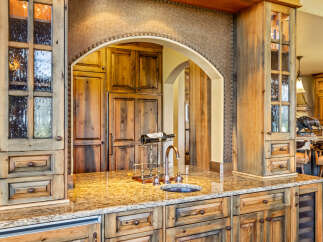 Experience luxury in this stunning kitchen featuring custom knotty alder cabinetry with decorative glass doors and a granite countertop.