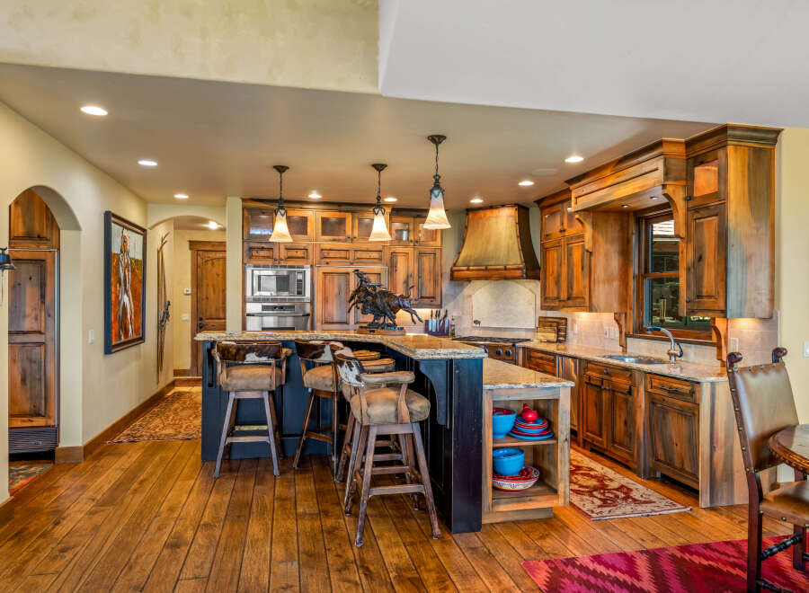 Experience rustic elegance in this stunning kitchen, featuring custom wood cabinetry, a granite-topped island with bar seating, and a striking copper range hood.