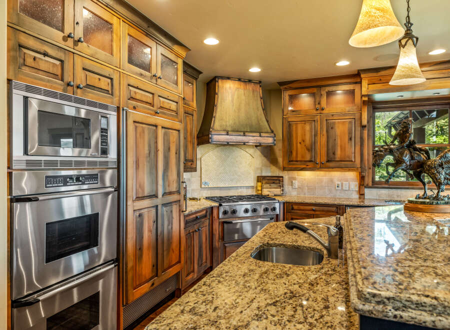Experience rustic elegance in this stunning kitchen, featuring custom knotty alder cabinetry with glass-front upper cabinets and a striking copper range hood.
