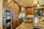 Experience rustic elegance in this stunning kitchen, featuring custom knotty alder cabinetry with glass-front upper cabinets and a striking copper range hood.