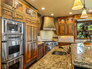Experience rustic elegance in this stunning kitchen, featuring custom knotty alder cabinetry with glass-front upper cabinets and a striking copper range hood.