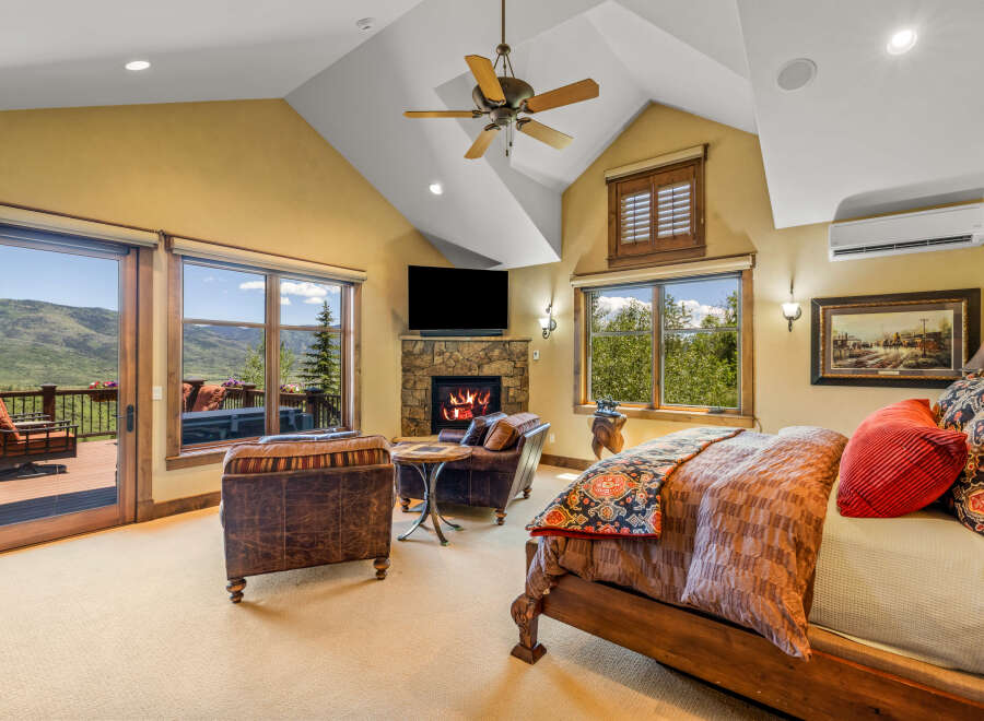 Experience luxury mountain living in this stunning bedroom featuring a cozy stone fireplace and breathtaking views from the private balcony.