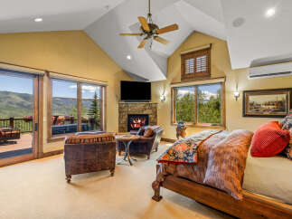 Experience luxury mountain living in this stunning bedroom featuring a cozy stone fireplace and breathtaking views from the private balcony.