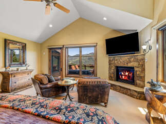 Experience luxury mountain living in this stunning bedroom featuring a cozy stone fireplace and breathtaking panoramic views from the large windows.