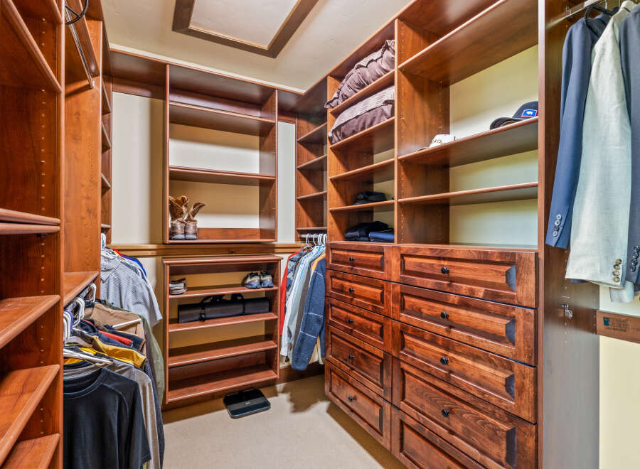 Step into this spacious walk-in closet, featuring custom cherry wood cabinetry and ample shelving for all your storage needs.