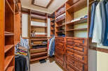 Step into this spacious walk-in closet, featuring custom cherry wood cabinetry and ample shelving for all your storage needs.