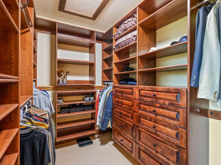Step into this spacious walk-in closet, featuring custom cherry wood cabinetry and ample shelving for all your storage needs.