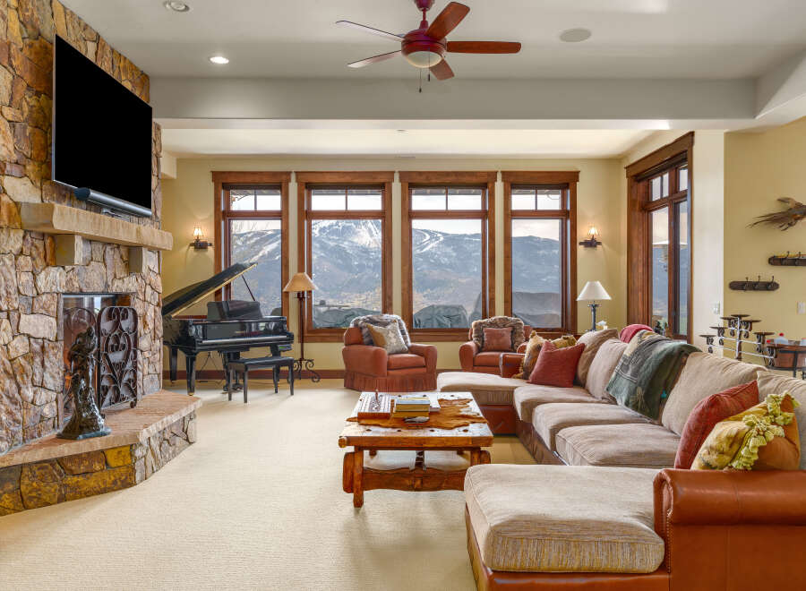 Experience luxury mountain living in this stunning great room, featuring a grand piano and a massive stone fireplace.