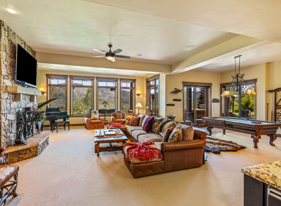 Experience luxury mountain living in this spacious great room, featuring a grand piano, a large stone fireplace, and a pool table for entertainment.