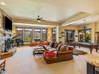 Experience luxury mountain living in this spacious great room, featuring a grand piano, a large stone fireplace, and a pool table for entertainment.