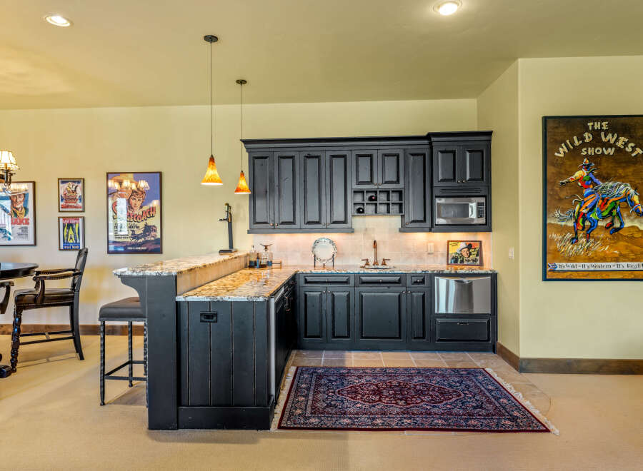 Step into a Western-themed entertainment space featuring a stylish bar with granite countertops and dark wood cabinetry.