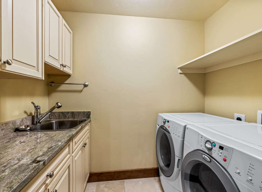 This spacious laundry room features a convenient utility sink with granite countertops and ample cabinet storage.