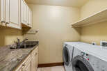 This spacious laundry room features a convenient utility sink with granite countertops and ample cabinet storage.