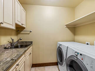 This spacious laundry room features a convenient utility sink with granite countertops and ample cabinet storage.
