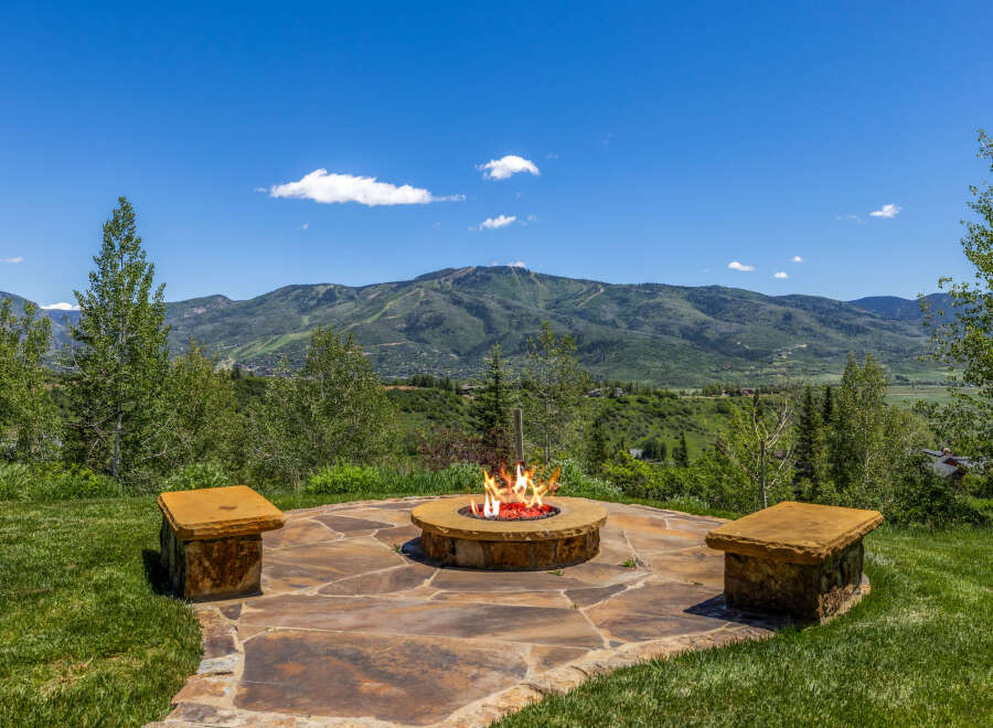Enjoy breathtaking mountain views from this stunning outdoor living space, complete with a cozy fire pit and stone seating.