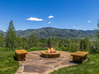 Enjoy breathtaking mountain views from this stunning outdoor living space, complete with a cozy fire pit and stone seating.