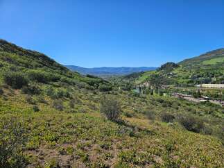 Discover breathtaking panoramic views from this elevated vantage point, overlooking a vibrant valley community nestled amongst rolling green hills.