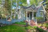 Charming light blue home with a welcoming front porch and white railings, nestled amongst mature trees.