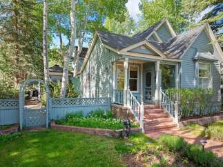 Charming light blue home with a welcoming front porch and white railings, nestled amongst mature trees.