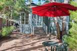 Enjoy outdoor living in this charming backyard featuring a red umbrella, a wrought iron table and chairs, and a brick patio perfect for al fresco dining.