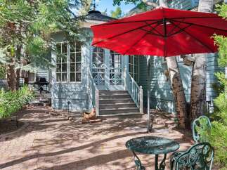 Enjoy outdoor living in this charming backyard featuring a red umbrella, a wrought iron table and chairs, and a brick patio perfect for al fresco dining.
