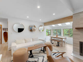 Experience modern living in this bright and airy open-concept space, featuring a comfortable sectional sofa, a live-edge coffee table, and a stylish dining area with ample natural light from skylights and large windows.