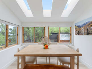 Experience natural light and stunning views in this dining area, featuring expansive skylights and large windows overlooking lush greenery.