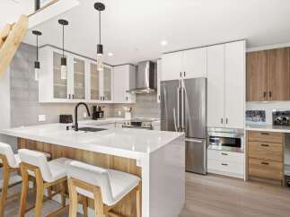 Experience modern living in this stunning kitchen featuring sleek white cabinetry, a spacious island with waterfall countertops, and elegant pendant lighting.