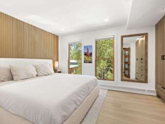 Experience modern comfort in this beautifully appointed bedroom, featuring a plush bed with crisp white linens and a striking slatted wood accent wall.