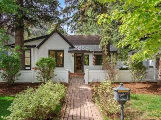 Charming white cottage with black trim and a welcoming brick pathway leading to the front door.
