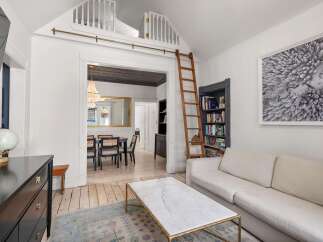 Discover this charming living space featuring a cozy sectional sofa, a marble-topped coffee table, and a built-in bookshelf with a unique ladder.
